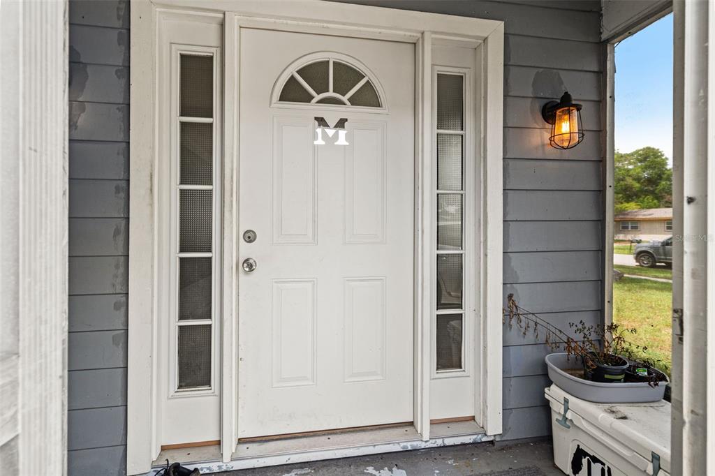 A white front door with a letter M and side windows sits on a porch — 4555 CYNTHIA LANE, SPRING HILL, FL