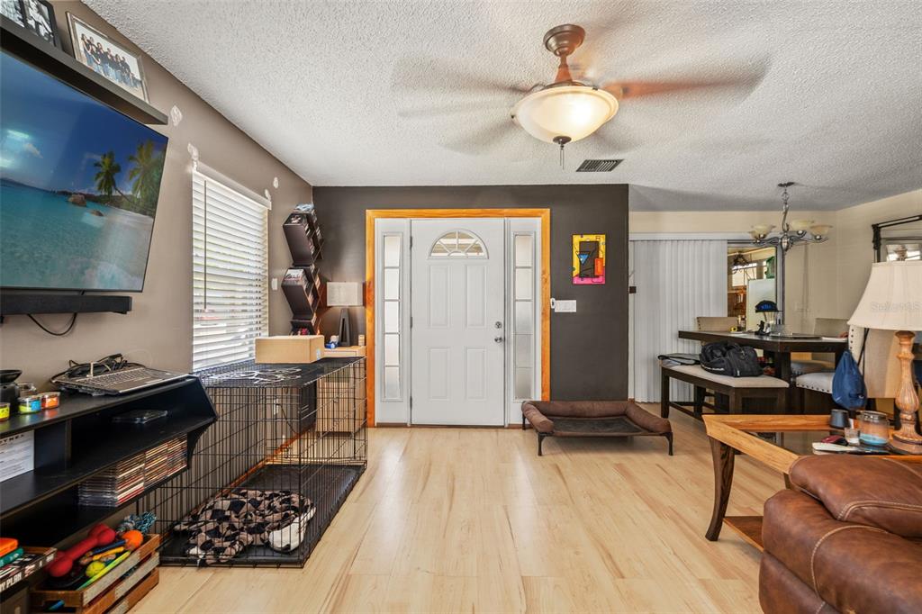 A living room with light wood flooring, a white front door, and a dog crate — 4555 CYNTHIA LANE, SPRING HILL, FL
