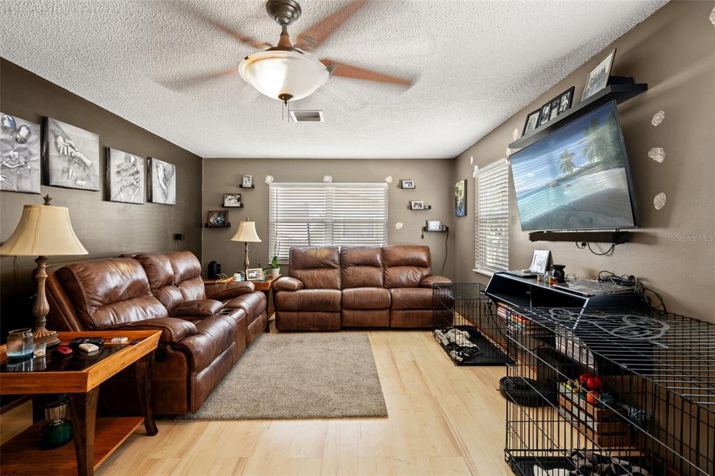A living room features brown leather sofas, light wood flooring, and a wall-mounted television — 4555 CYNTHIA LANE, SPRING HILL, FL