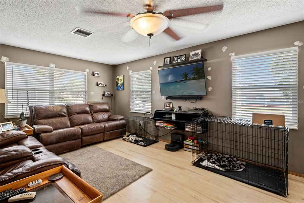A living room features brown leather sofas, a television, and two large dog crates — 4555 CYNTHIA LANE, SPRING HILL, FL