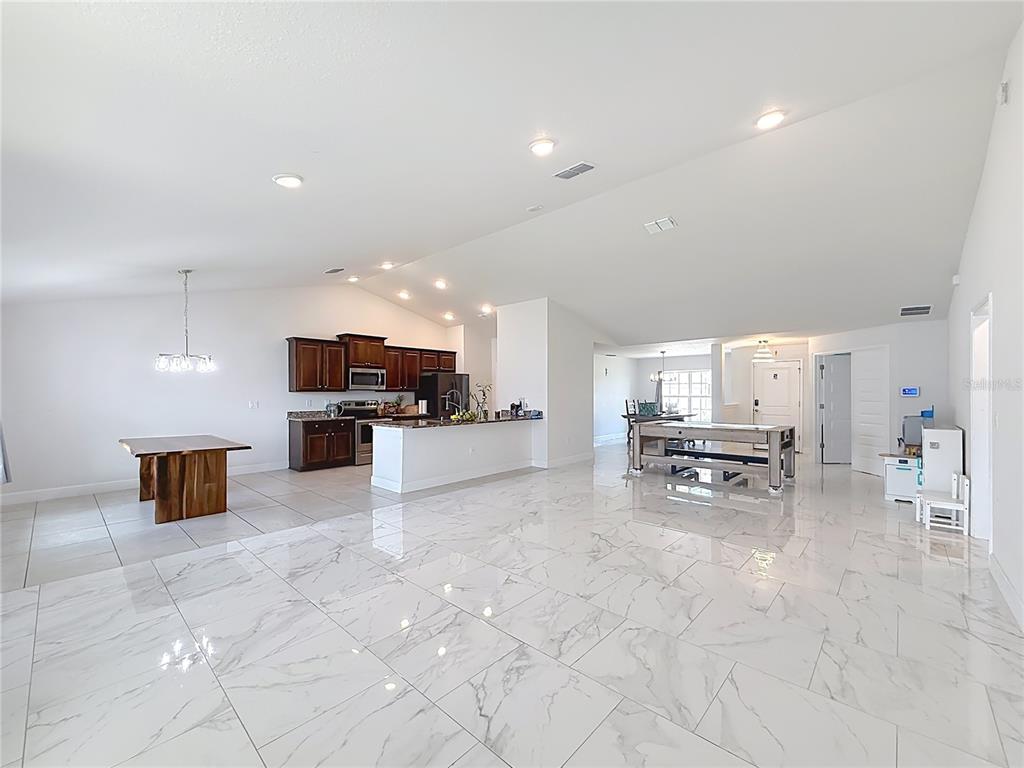 An open-concept living area features white marble-look tile flooring, a kitchen with dark cabinetry, and vaulted ceilings — 5108 SW 90TH PLACE, OCALA, FL