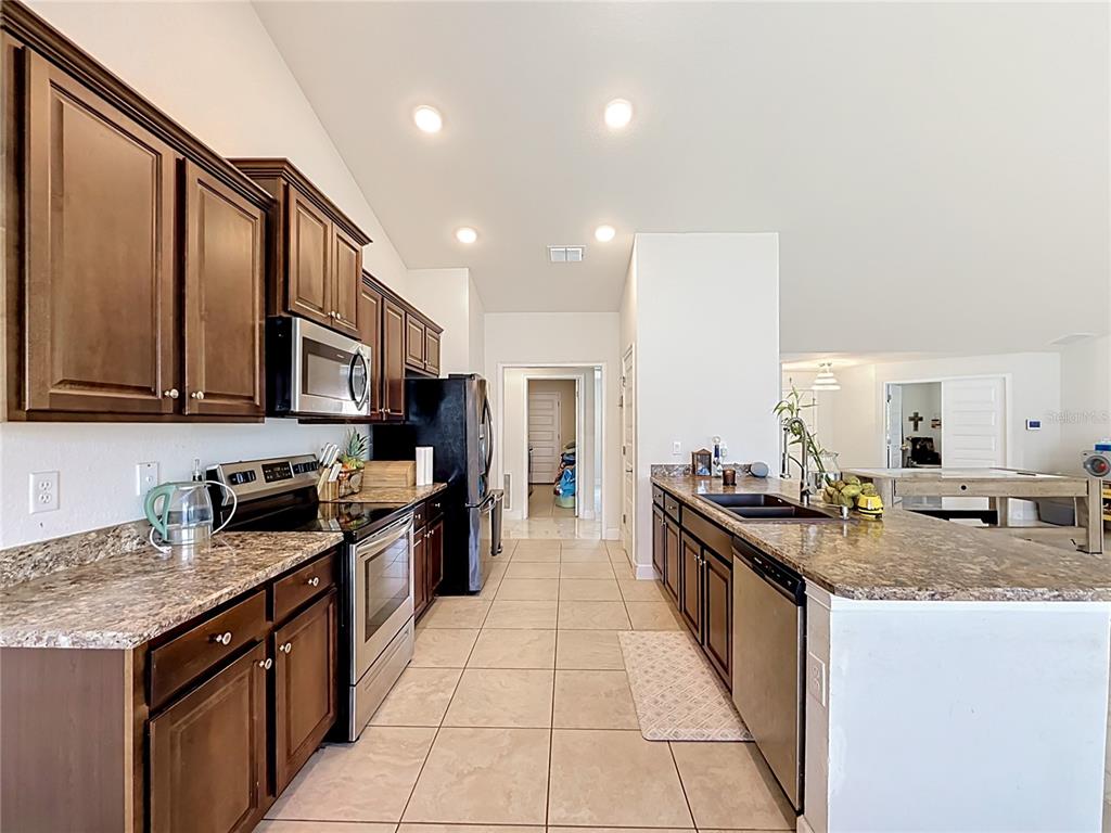 A kitchen features dark wood cabinets, granite countertops, stainless steel appliances, and tile flooring — 5108 SW 90TH PLACE, OCALA, FL