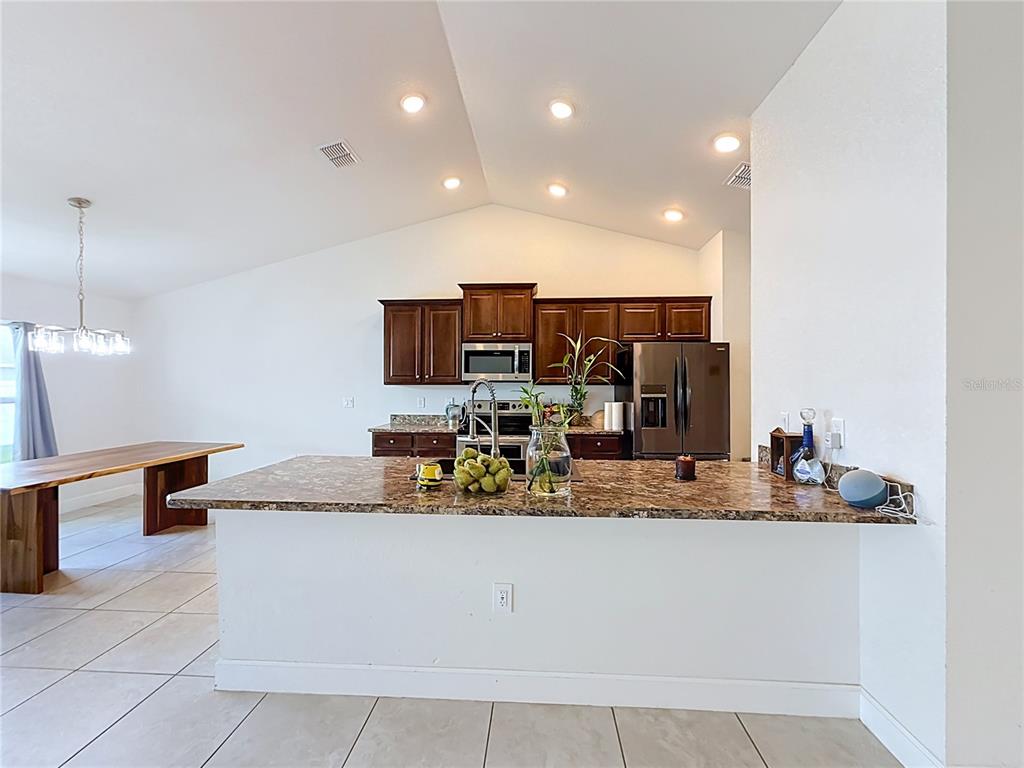 A kitchen features dark wood cabinets, granite countertops, a central island, and stainless steel appliances — 5108 SW 90TH PLACE, OCALA, FL