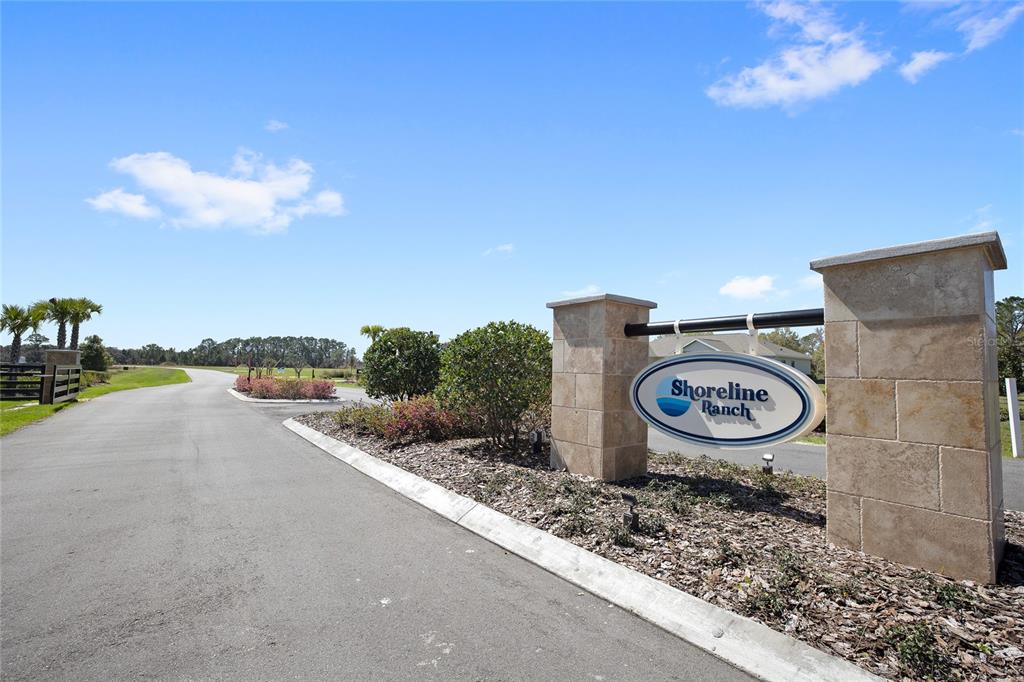 A stone entrance sign for Shoreline Ranch stands beside a paved road under a blue sky — 38361 LAKE MEADOW COURT, UMATILLA, FL