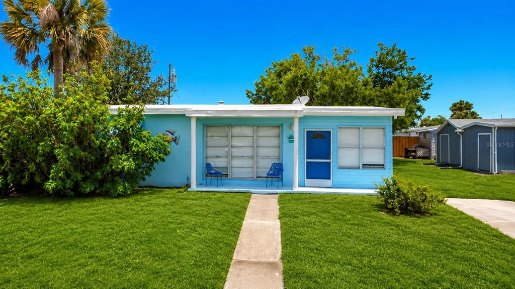 A light blue single-story house features a concrete walkway, two blue chairs, and a lawn — 8594 BUMFORD AVENUE, NORTH PORT, FL