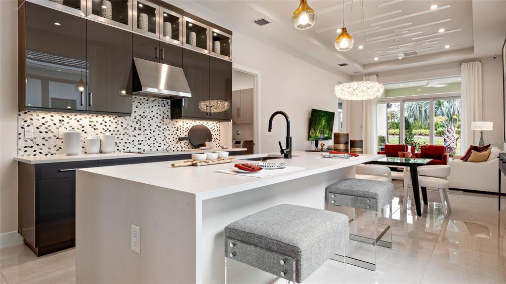 A modern kitchen features dark glossy cabinets, a white quartz island, and gray upholstered stools — 423 VERONA WAY, LADY LAKE, FL