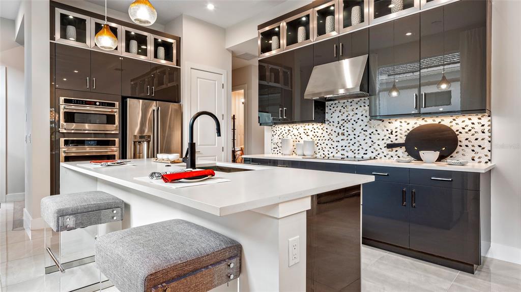 A modern kitchen features dark glossy cabinetry, a white quartz island, and two gray stools — 423 VERONA WAY, LADY LAKE, FL