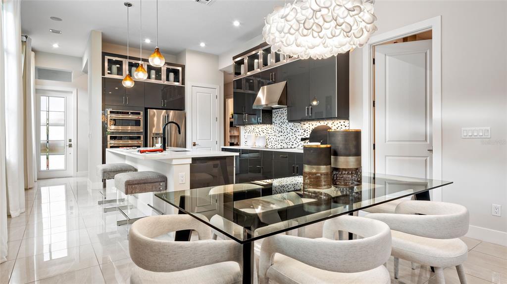 A modern kitchen features dark cabinetry, a glass dining table, and white tile flooring — 423 VERONA WAY, LADY LAKE, FL