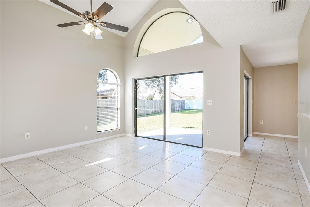 A living room with vaulted ceilings, tile flooring, a ceiling fan, and sliding glass doors — 11943 BLACKHEATH CIRCLE, ORLANDO, FL