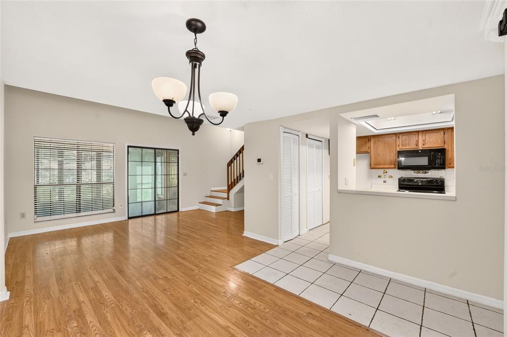 A living room with hardwood floors, a chandelier, stairs, and an open kitchen pass-through — 924 SW 57TH DRIVE, GAINESVILLE, FL