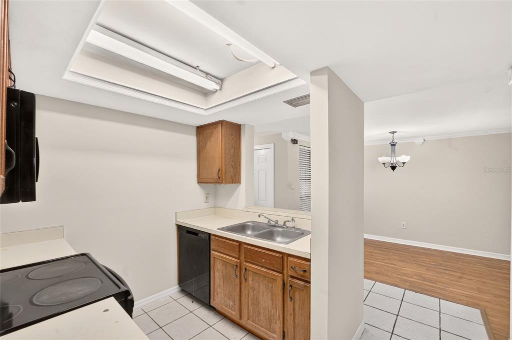 A kitchen with wood cabinets, a double sink, and tile flooring opens to a dining area — 924 SW 57TH DRIVE, GAINESVILLE, FL
