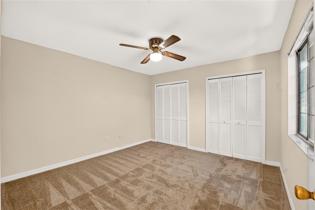 A bedroom with beige walls, brown carpet, a ceiling fan, and two white louvered closets — 924 SW 57TH DRIVE, GAINESVILLE, FL