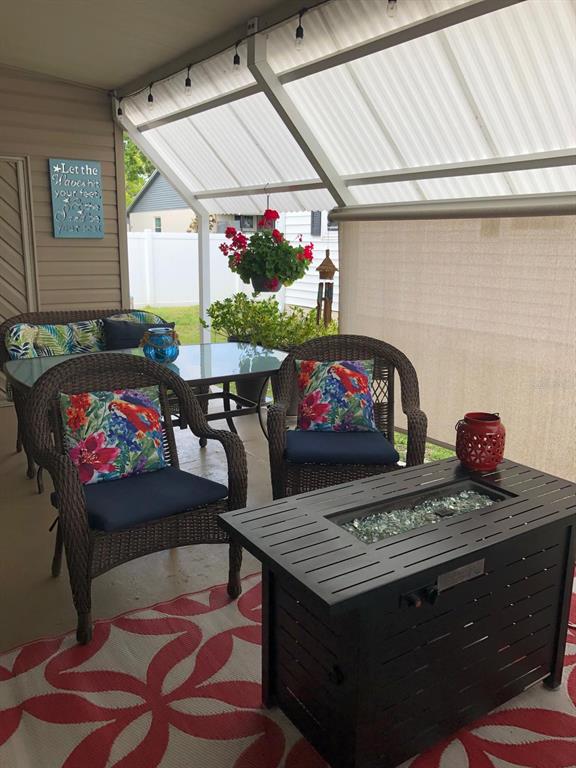 A covered patio features wicker furniture, a fire pit, and a dining table on a rug — 1100 BELCHER ROAD S UNIT 18, LARGO, FL