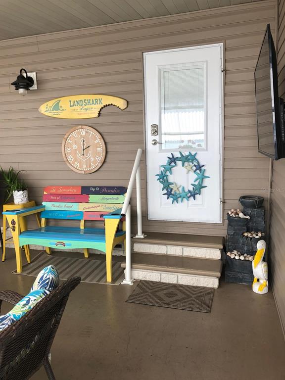 A covered porch features a colorful bench, a starfish wreath on the door, and decor — 1100 BELCHER ROAD S UNIT 18, LARGO, FL