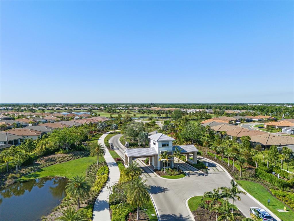 An aerial view of a gated community entrance with a guardhouse, palm trees, and houses — 14833 MONTELLO WAY, BRADENTON, FL