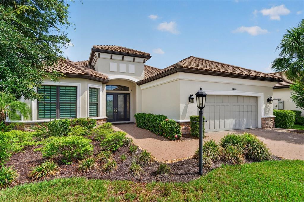 A single-story house with a tile roof, beige stucco exterior, and a two-car garage — 14833 MONTELLO WAY, BRADENTON, FL