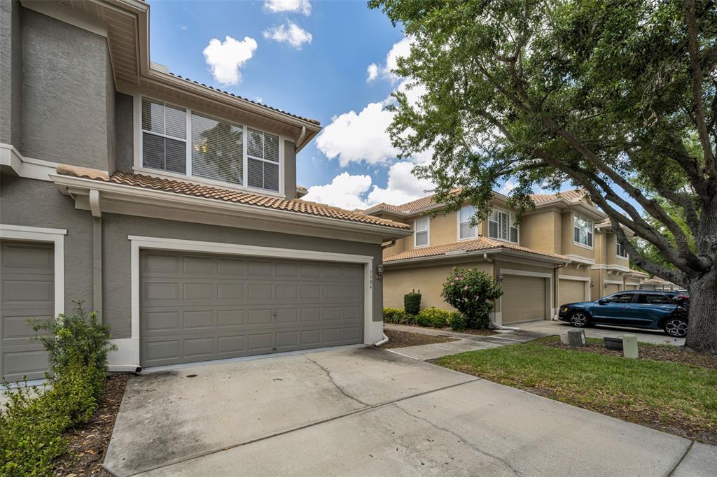 A two-story townhouse with a gray stucco exterior, a two-car garage, and a concrete driveway — 3304 COVERED BRIDGE DRIVE E, DUNEDIN, FL