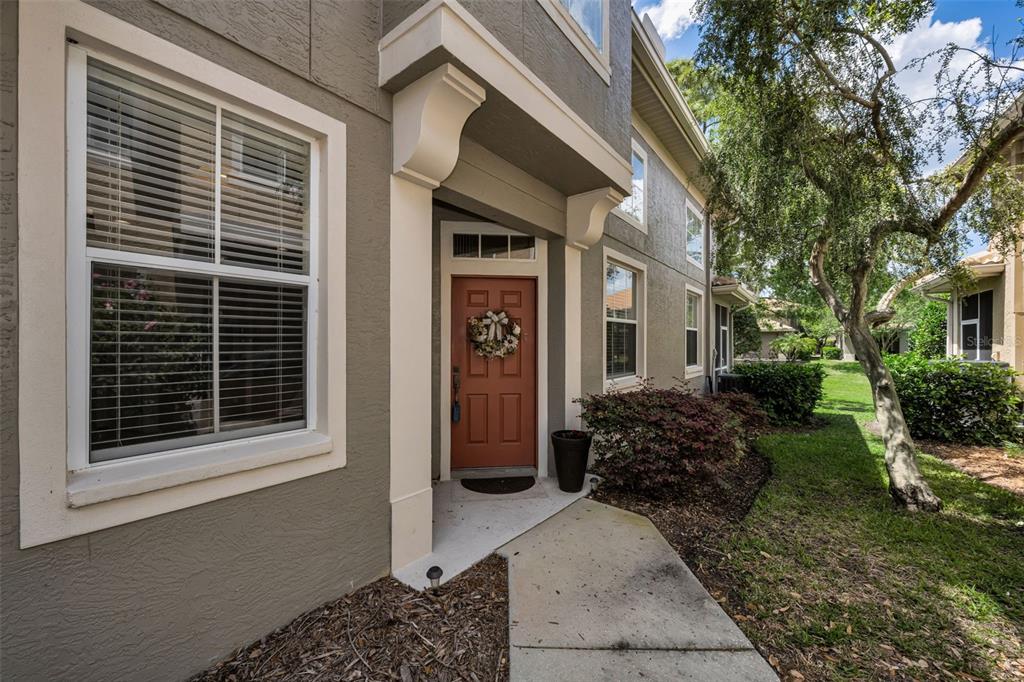 A tan two-story townhouse exterior features a red front door and a concrete walkway — 3304 COVERED BRIDGE DRIVE E, DUNEDIN, FL