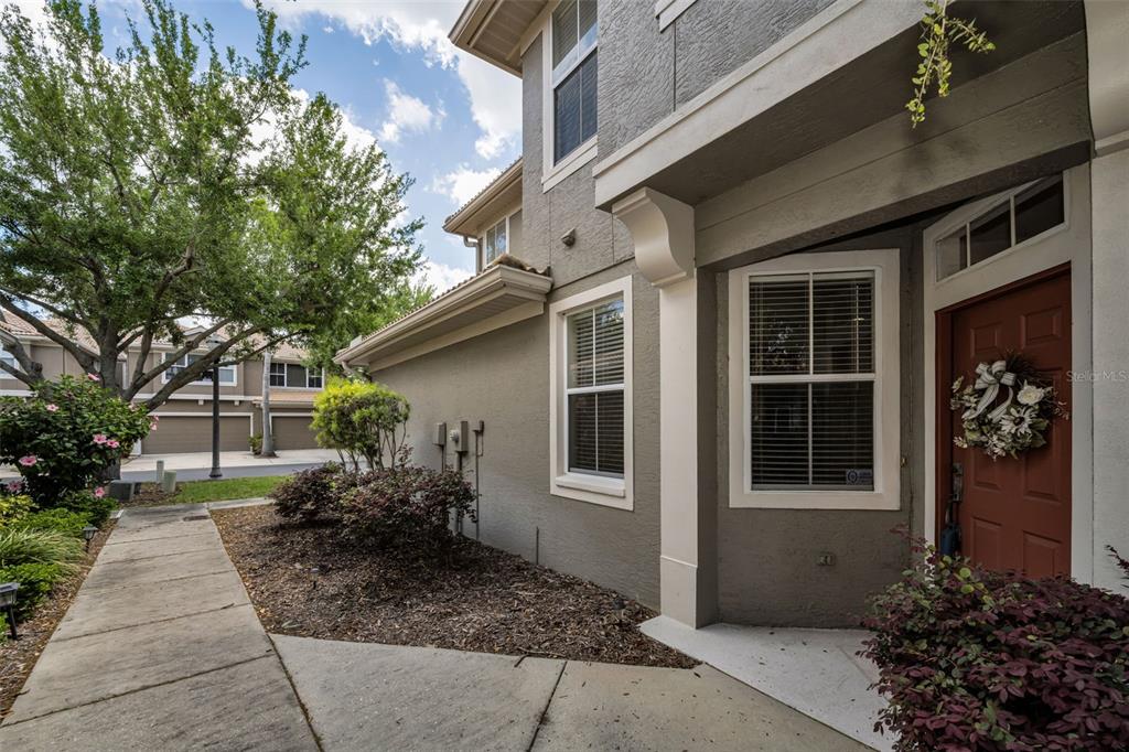 A concrete walkway leads to the entrance of a two-story gray stucco townhouse — 3304 COVERED BRIDGE DRIVE E, DUNEDIN, FL