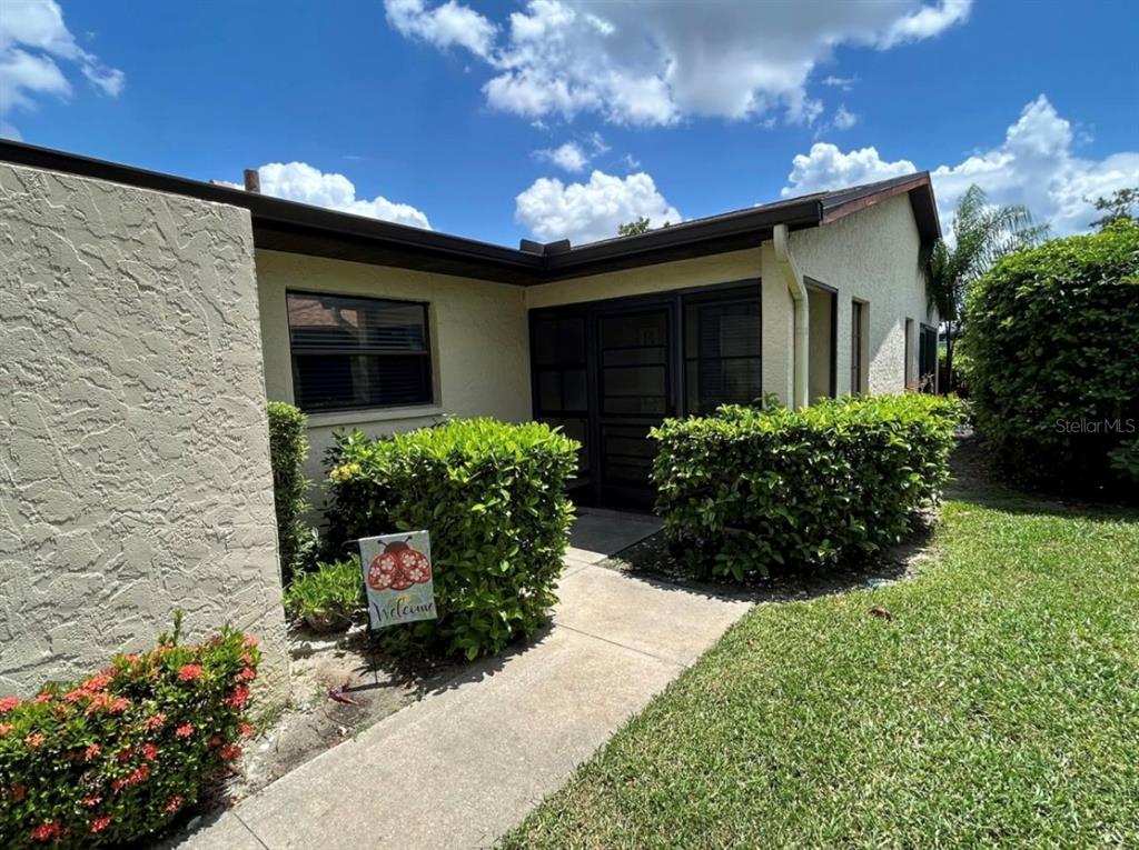 A beige stucco house exterior features a screened entryway, a concrete walkway, and manicured hedges — 3312 VIVIENDA BOULEVARD, BRADENTON, FL