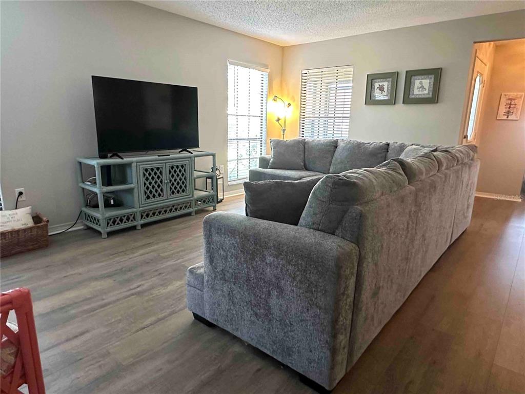 A living room features a gray sectional sofa, a television on a blue console, and wood-look flooring — 3312 VIVIENDA BOULEVARD, BRADENTON, FL