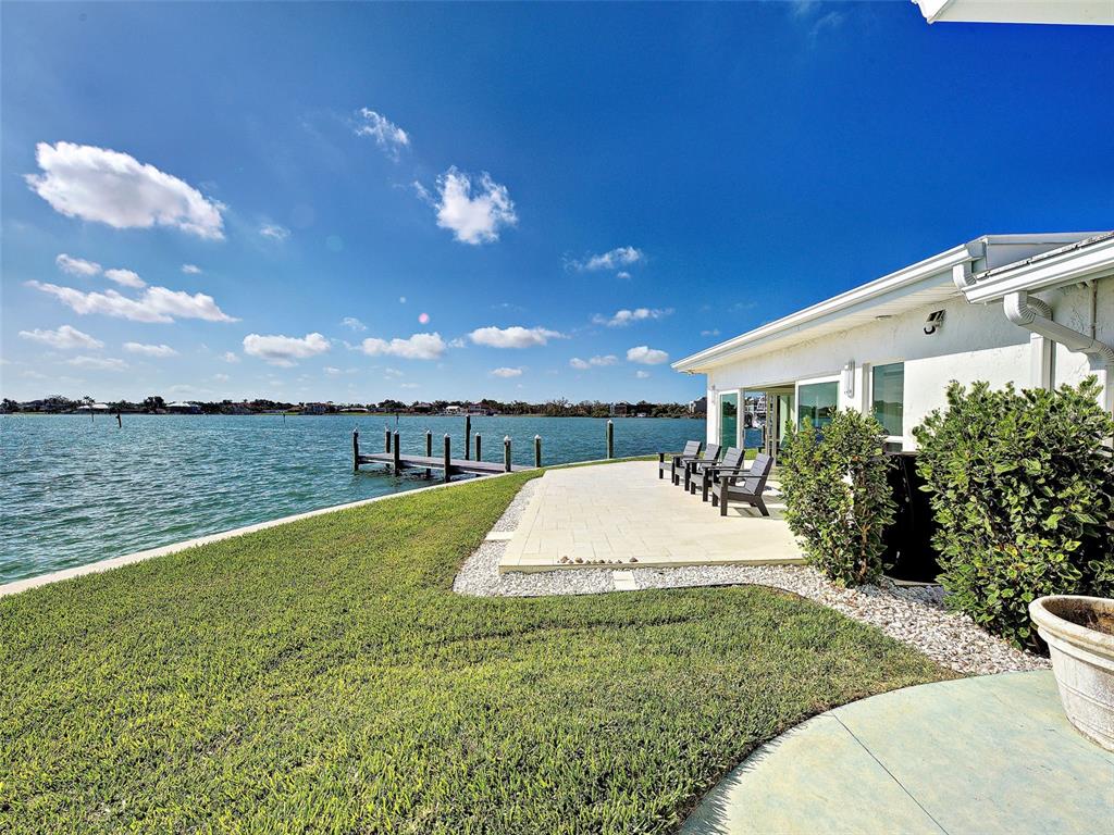 A paved patio sits beside a grassy lawn overlooking a waterfront canal with a dock — 885 WHITE CAP CIRCLE UNIT 34, VENICE, FL