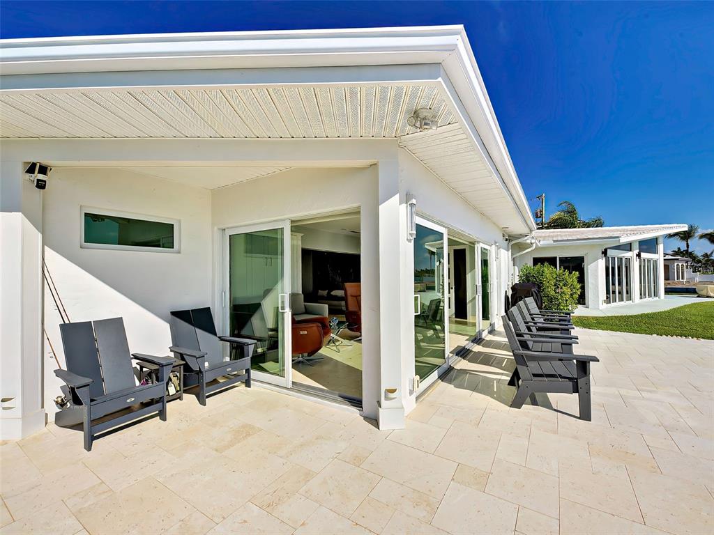 A covered patio with stone flooring and dark chairs sits outside a house with sliding doors — 885 WHITE CAP CIRCLE UNIT 34, VENICE, FL