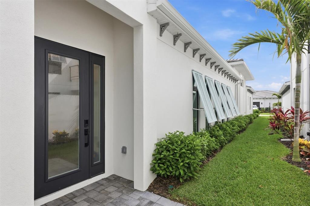 A white exterior wall features a dark door, a row of windows with shutters, and landscaping — 5931 CAT CLAW LANE, BRADENTON, FL