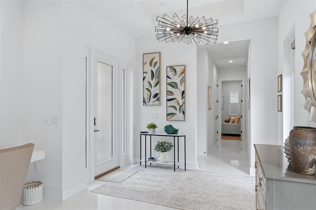 A bright entryway features a modern chandelier, a console table, and two framed leaf prints — 5931 CAT CLAW LANE, BRADENTON, FL