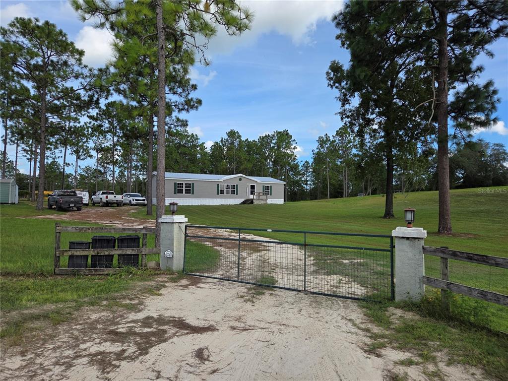 A single-story manufactured home sits behind a gated entrance on a grassy, tree-lined lot — 13030 SE 21ST PLACE, MORRISTON, FL