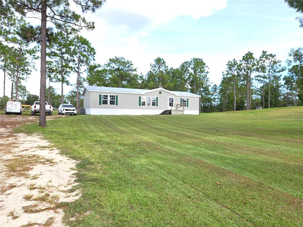 A single-story manufactured home sits on a large, grassy lot surrounded by pine trees — 13030 SE 21ST PLACE, MORRISTON, FL