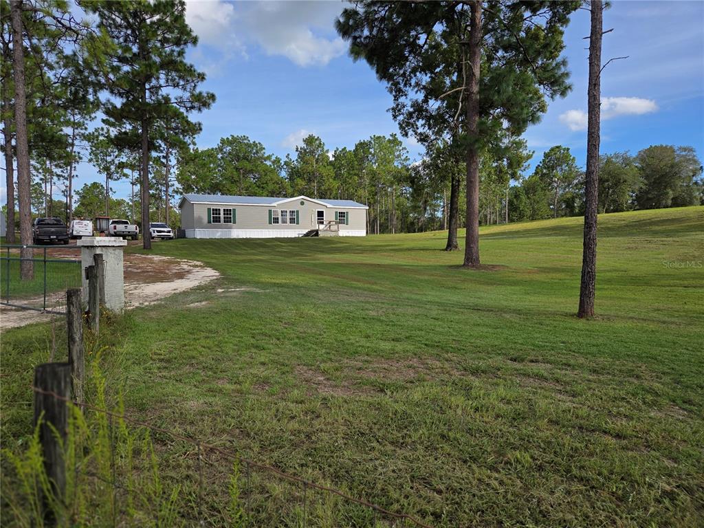 A single-story manufactured home sits on a grassy, tree-lined lot with several parked vehicles — 13030 SE 21ST PLACE, MORRISTON, FL