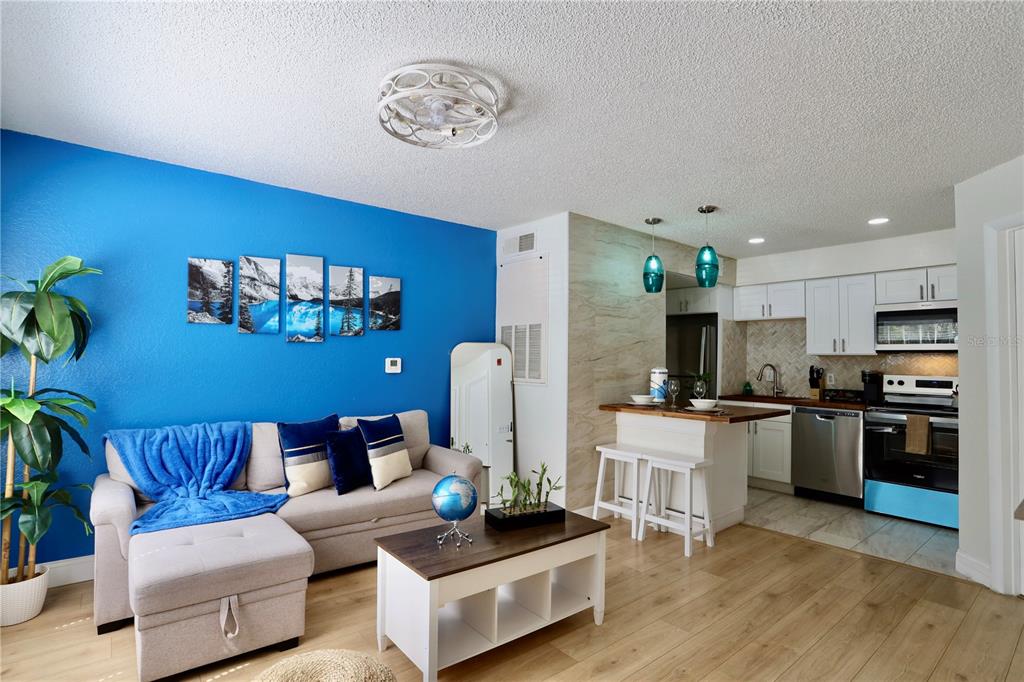 A living room with a blue accent wall, sectional sofa, and an open-concept kitchen — 2207 ANTIGUA PLACE UNIT 717, KISSIMMEE, FL