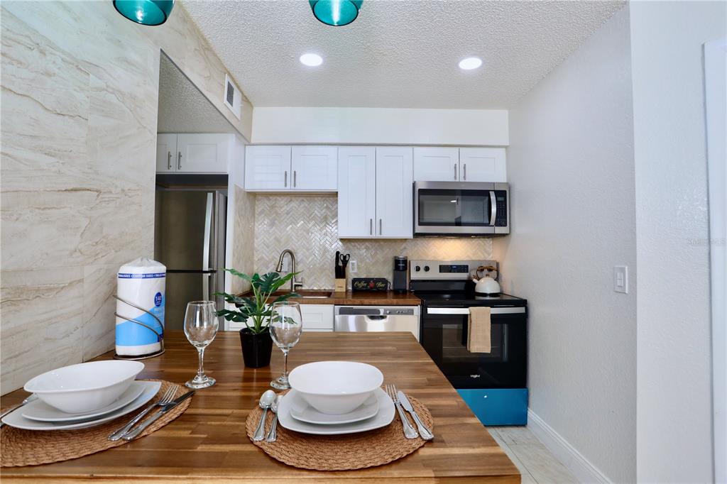 A kitchen features white cabinets, stainless steel appliances, a herringbone backsplash, and a wooden dining table — 2207 ANTIGUA PLACE UNIT 717, KISSIMMEE, FL