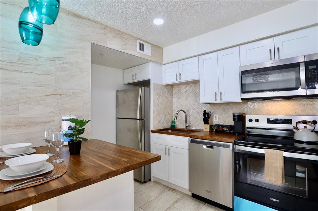 A kitchen features white cabinets, stainless steel appliances, a wood countertop, and a breakfast bar — 2207 ANTIGUA PLACE UNIT 717, KISSIMMEE, FL