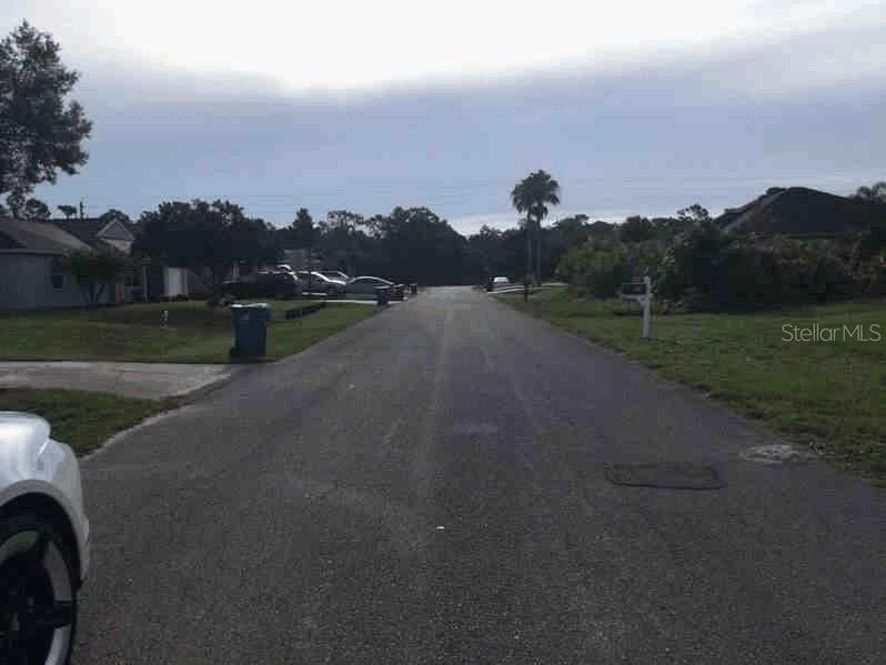 A paved residential street stretches forward with houses, parked cars, and trees on both sides — 1661 PALATKA ROAD SE, PALM BAY, FL