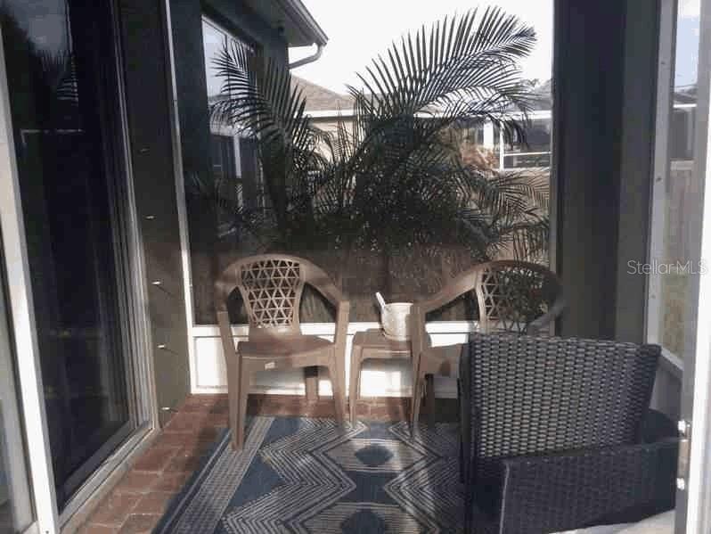 A screened-in patio features two plastic chairs, a small side table, and a patterned rug — 1661 PALATKA ROAD SE, PALM BAY, FL