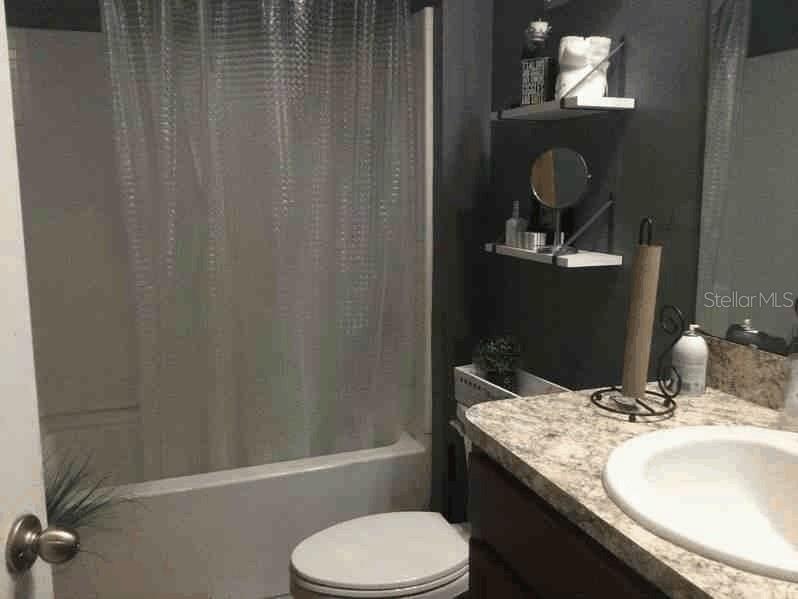 A bathroom features a shower-tub combo, a toilet, and a vanity with a stone countertop — 1661 PALATKA ROAD SE, PALM BAY, FL