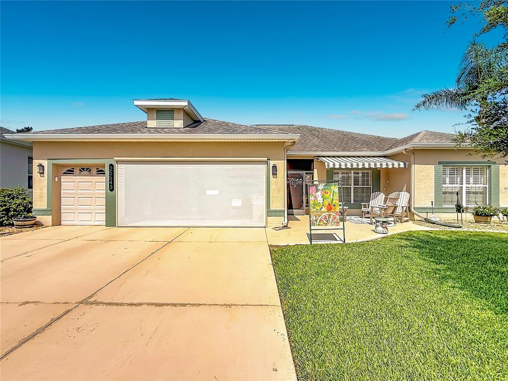 A single-story house with a two-car garage, a tan stucco exterior, and a front lawn — 25543 MAUREPAS LANE, LEESBURG, FL