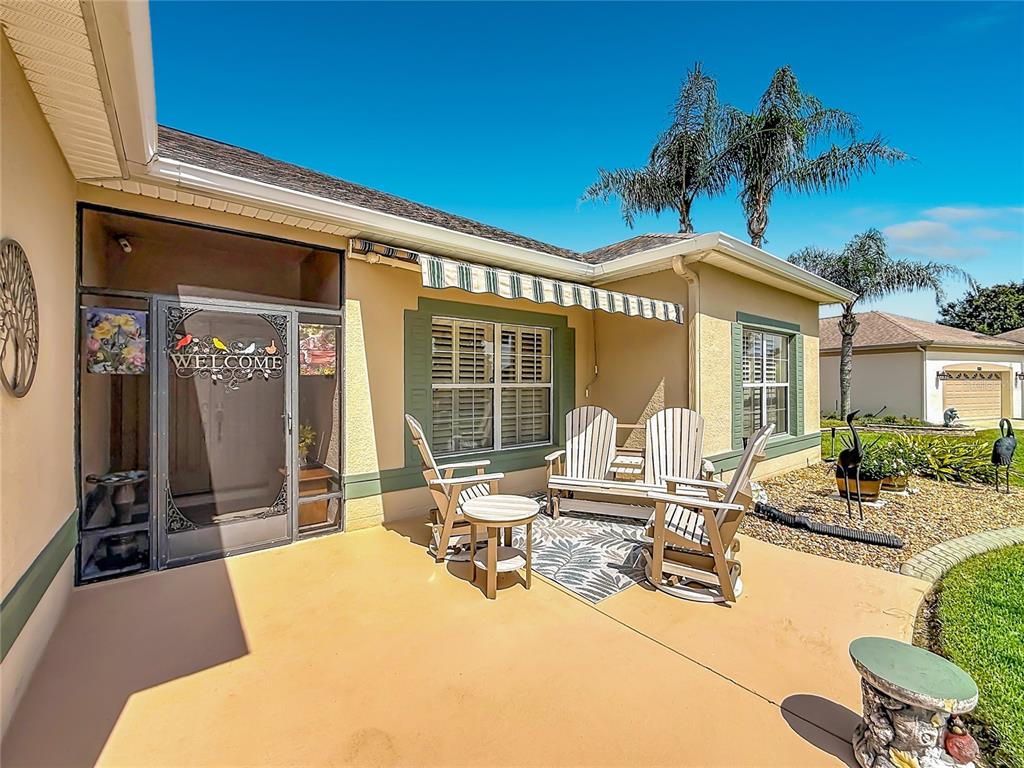 A patio with outdoor furniture, a screen door, and a striped awning on a house — 25543 MAUREPAS LANE, LEESBURG, FL