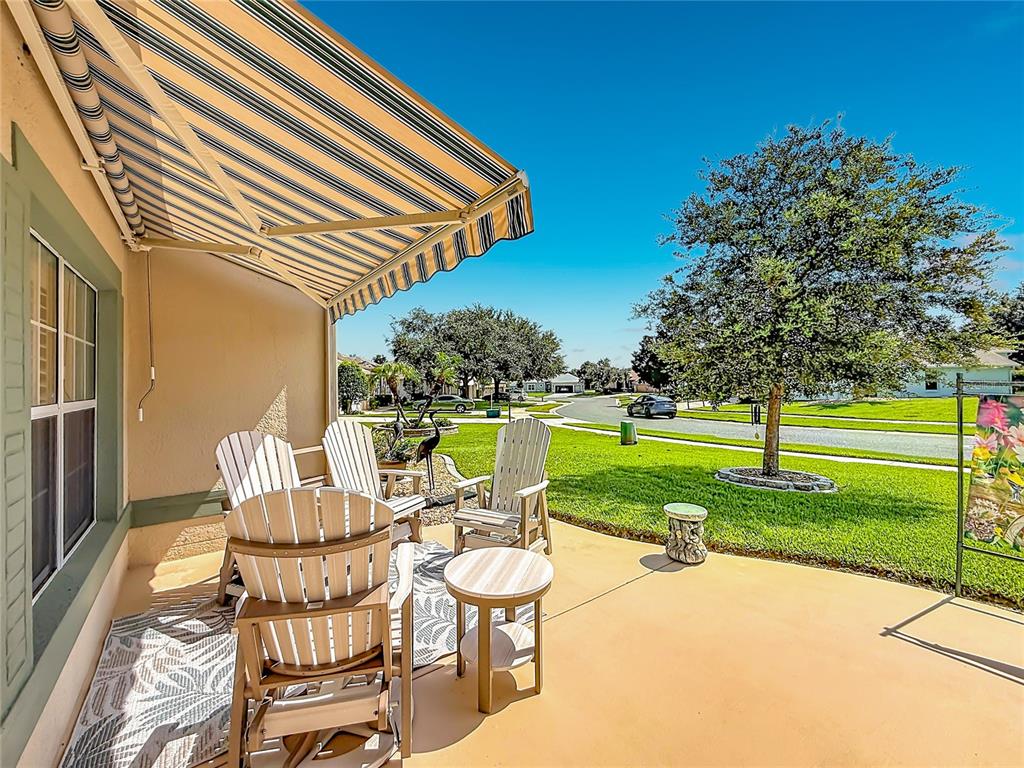 A covered patio with outdoor chairs and a striped awning overlooks a suburban lawn — 25543 MAUREPAS LANE, LEESBURG, FL