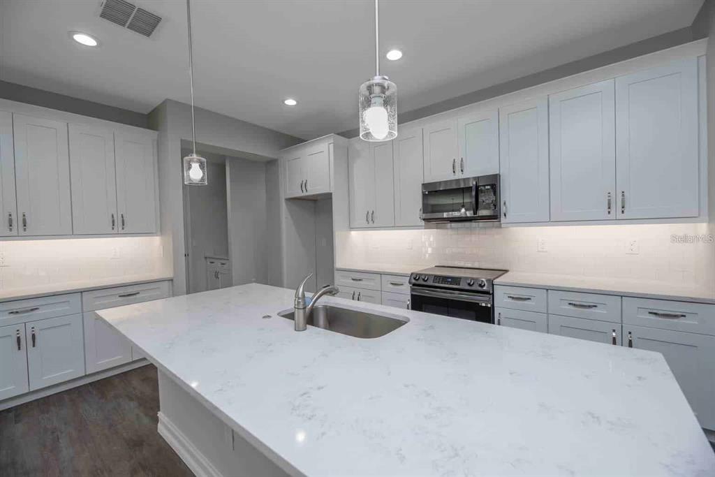 A modern kitchen features light gray cabinets, white quartz countertops, and a large central island — 1794 NW 83RD LOOP, OCALA, FL