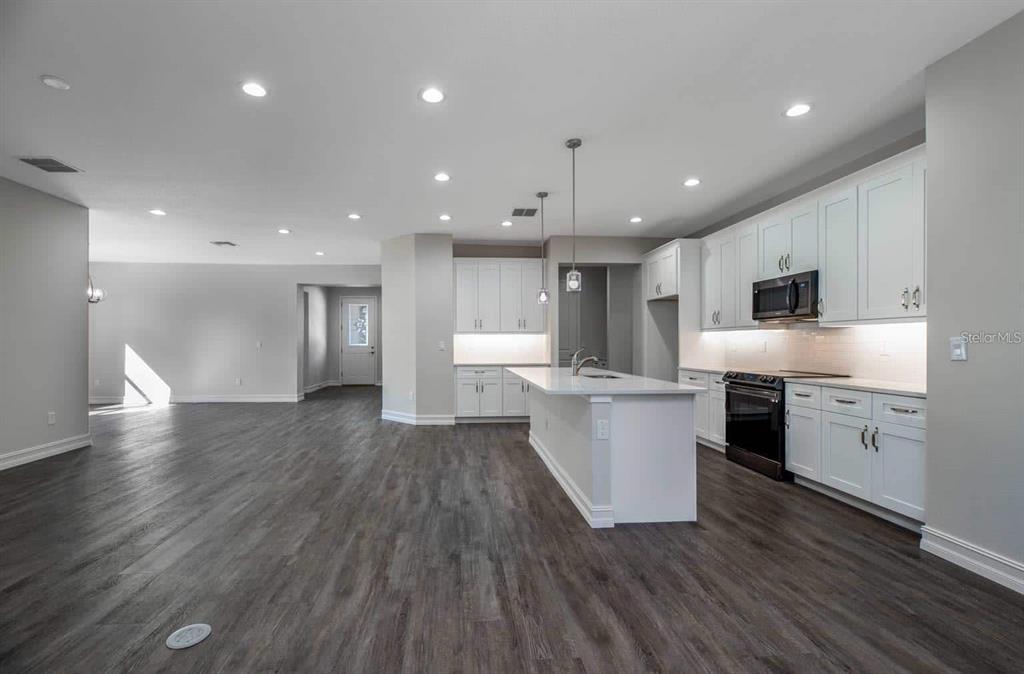 A modern kitchen with white cabinets and a central island opens into a living area — 1794 NW 83RD LOOP, OCALA, FL