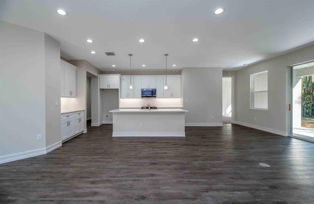 A modern kitchen features white cabinetry, a central island, and dark wood-look flooring — 1794 NW 83RD LOOP, OCALA, FL