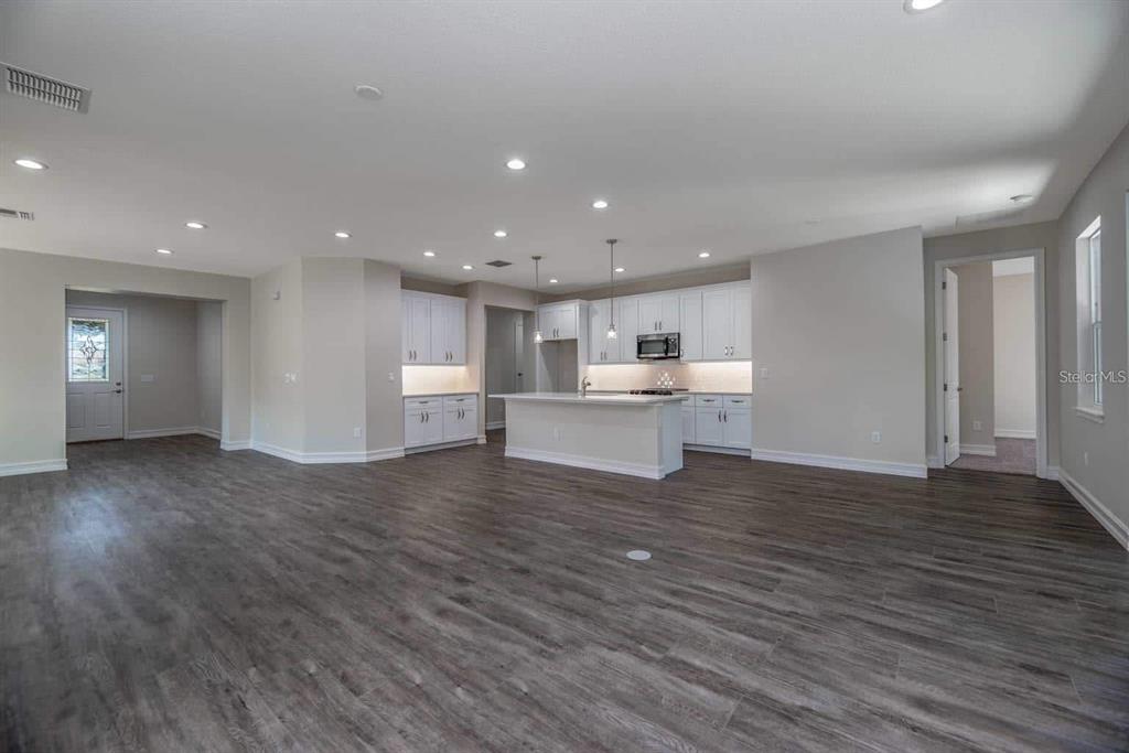 An open-concept kitchen and living area features white cabinetry, a center island, and wood-look flooring — 1794 NW 83RD LOOP, OCALA, FL