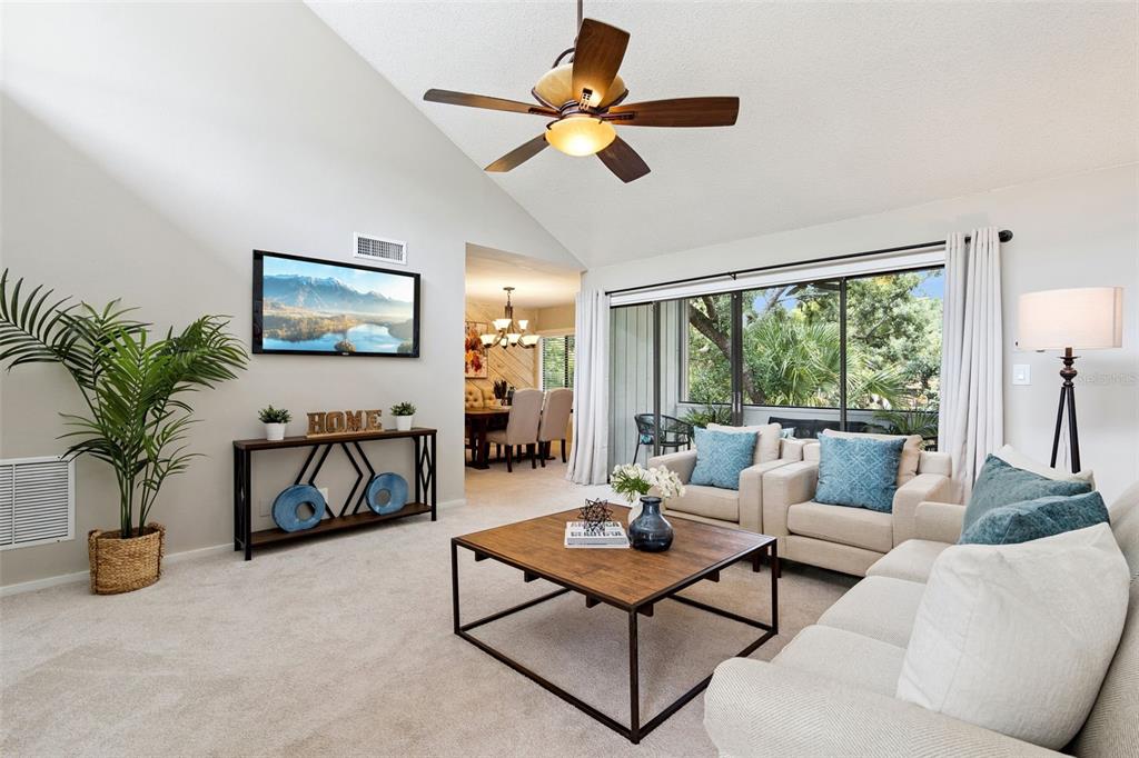 A living room features a vaulted ceiling, a ceiling fan, carpet, and sliding glass doors — 203 CROWN OAKS WAY UNIT 203, LONGWOOD, FL