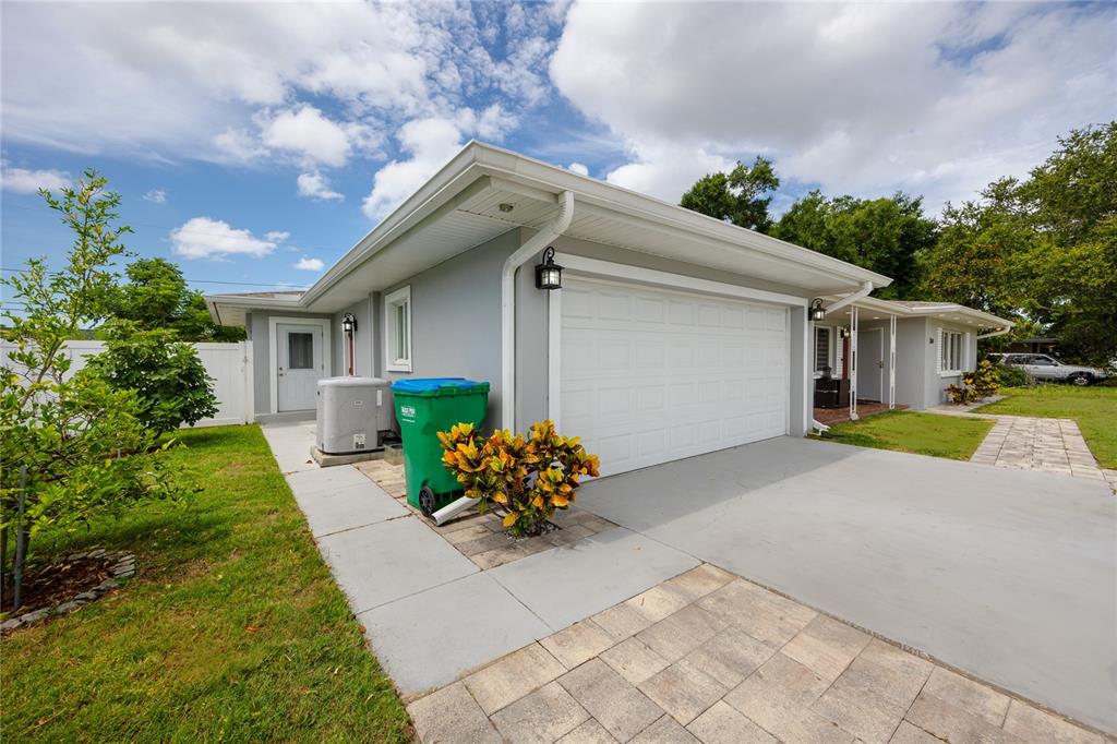 A gray house exterior features a white garage door, a green trash bin, and landscaping — 1833 HUNT LANE, CLEARWATER, FL