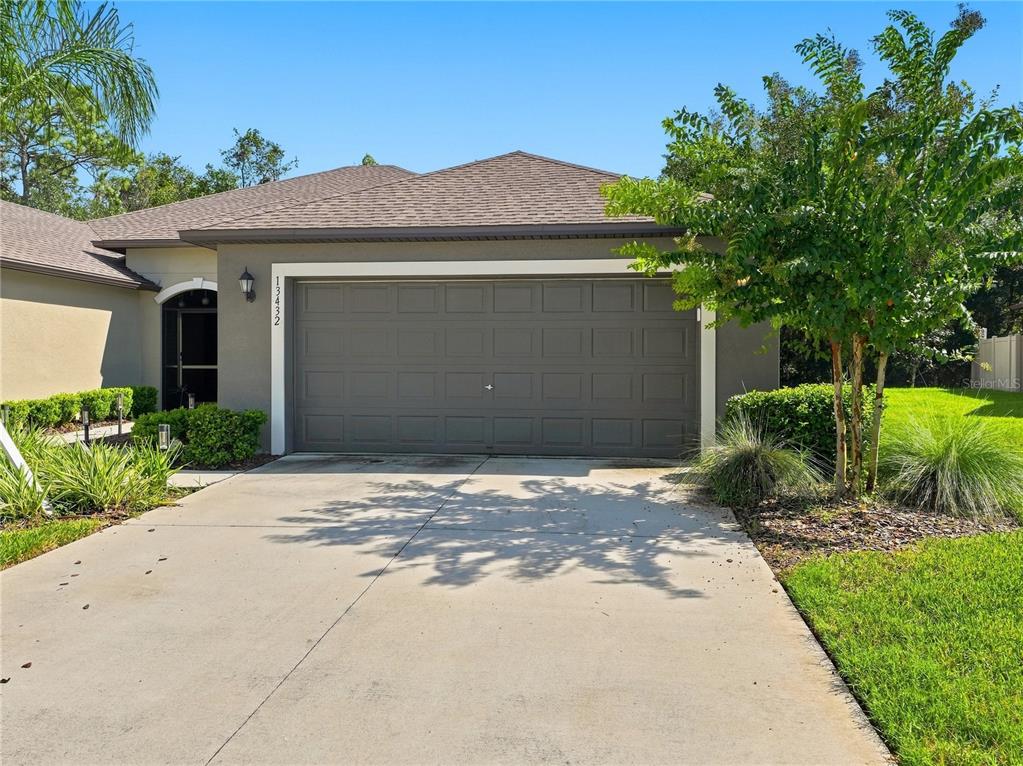 A concrete driveway leads to a two-car garage with a dark gray door — 13432 CREST LAKE DRIVE, HUDSON, FL