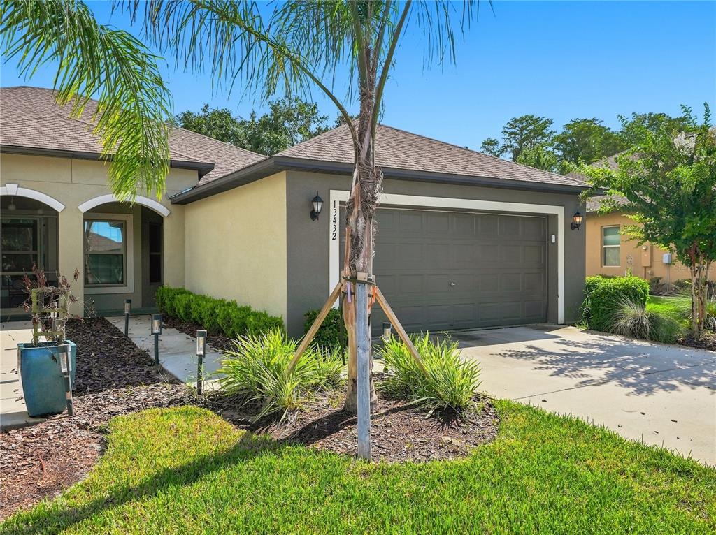 A single-story house exterior features a two-car garage, a palm tree, and a landscaped yard — 13432 CREST LAKE DRIVE, HUDSON, FL