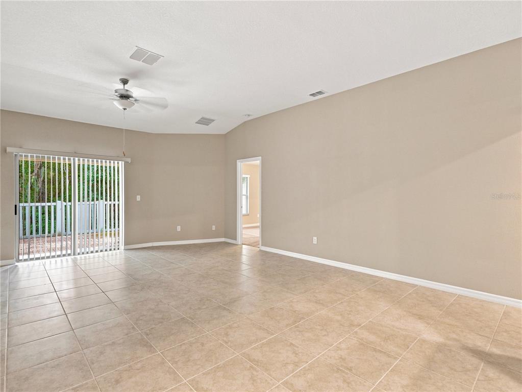 A spacious living room features beige tile flooring, neutral walls, and sliding glass patio doors — 13432 CREST LAKE DRIVE, HUDSON, FL